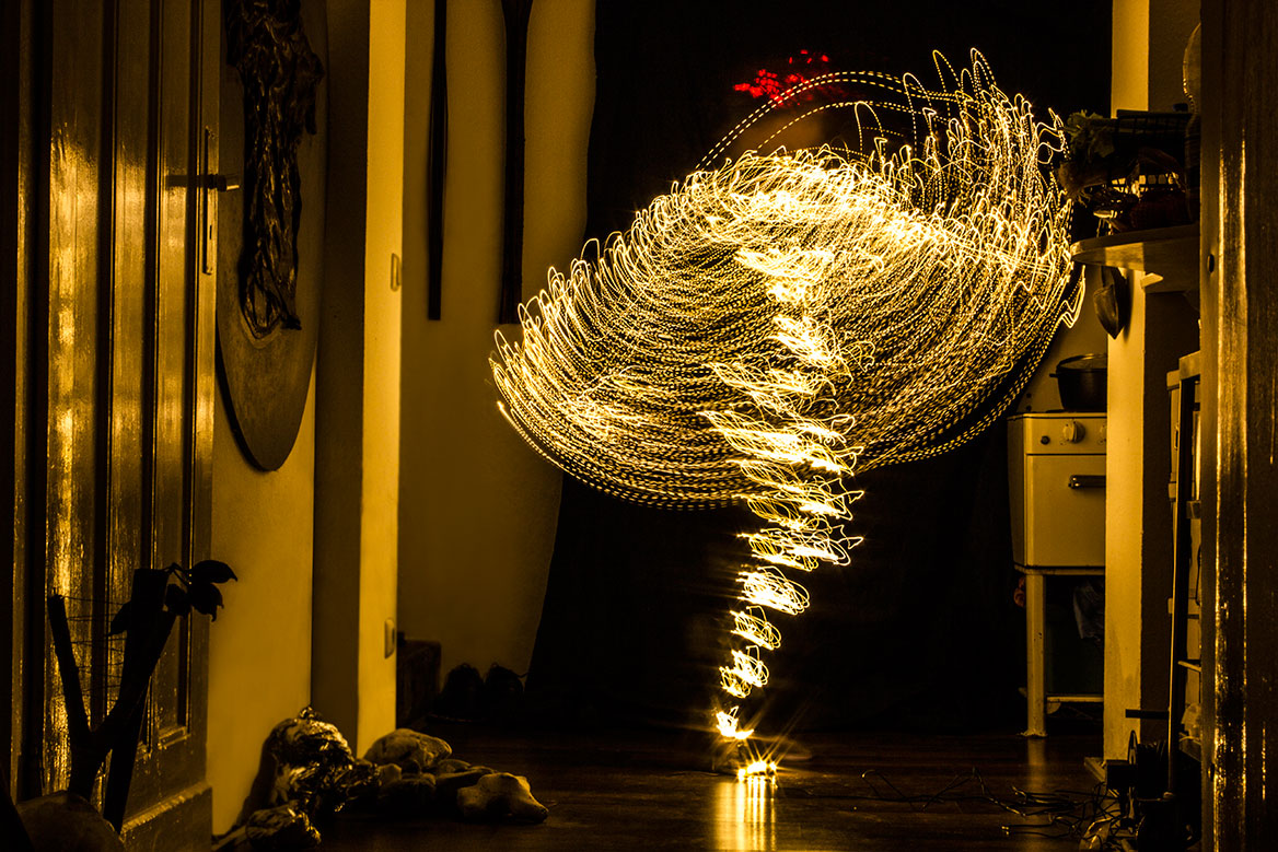 Fotografische Licht-Inszenierung, Einstellung 3. Eine Frau erstrahlt durch Lichtspuren, die durch Langzeitbelichtung die Körperbewegungen nachzeichnen. Die Lichtspuren werden filigraner und überschneiden sich stärker.